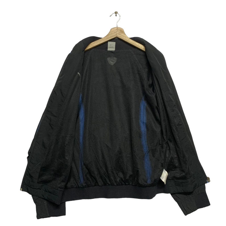 May include: A black windbreaker jacket with blue accents on the inside. The jacket has a zipper closure and a stand-up collar.