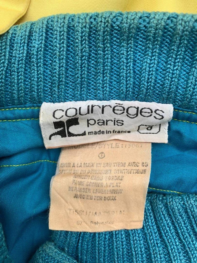 May include: A blue and yellow knitted sweater with a white tag that reads "courr&egrave;ges paris made in france" and "MODEL/STYLE: 15067". The tag also includes washing instructions in French.
