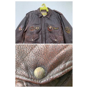 May include: A brown leather bomber jacket with multiple patches, including a U.S. Air Force patch, a  "U.S. Air Force" patch, and a "U.S. Army" patch. The jacket has a zipper closure and two pockets.