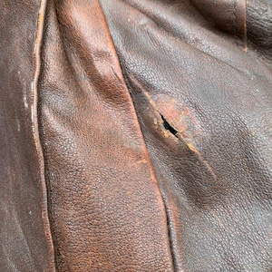 May include: Close-up of a brown leather jacket with a small tear in the fabric.