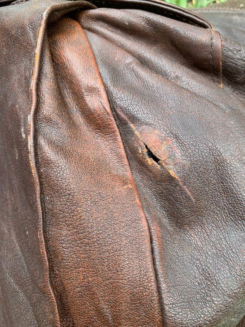 May include: Close-up of a brown leather jacket with a small tear in the fabric.