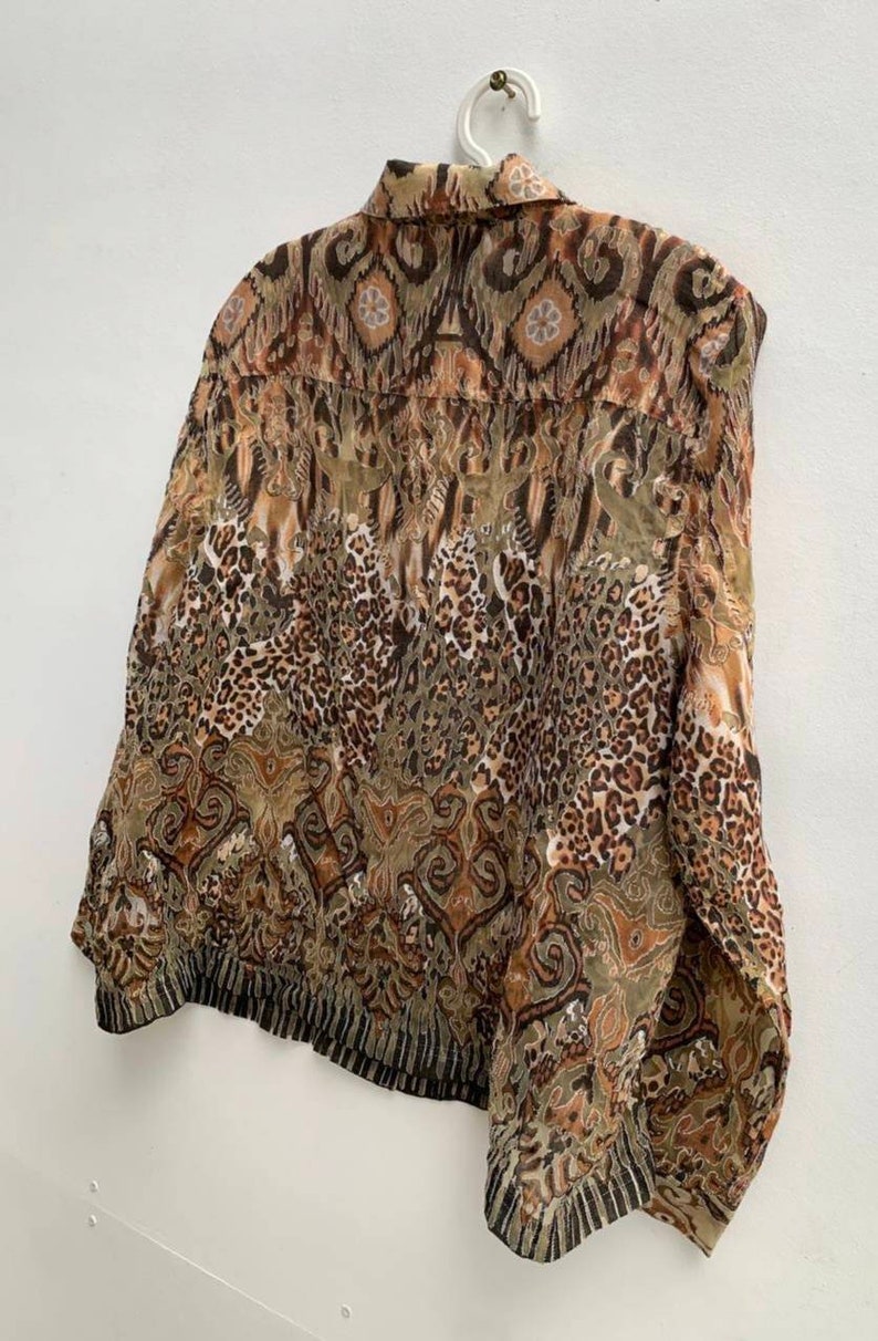 May include: A brown and green patterned shirt with a collared neckline and long sleeves. The shirt has a geometric and animal print design.