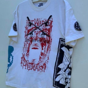 May include: White t-shirt with a graphic print of a skull with crossed skateboards and the text "Don't mess with Texas". The shirt also has a graphic print of a broken window with the text "HE" on the right side.
