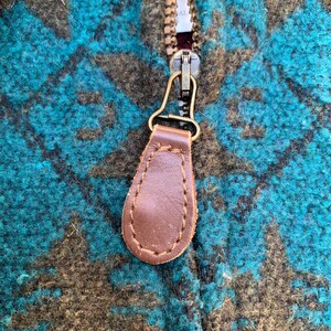 May include: Close-up of a brown leather zipper pull with a brass zipper slider. The zipper pull is attached to a blue and brown patterned fabric.