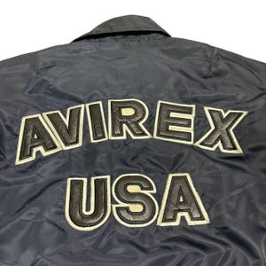 Vintage Avirex MA 1 Bomber Jacket Navy USA Flight Jacket 90s Streetwear Military Jacket Classic Zip Up Nylon Bomber Coat For Men And Women Rare Avirex USA Outerwear Piece With Iconic Back Logo Design.