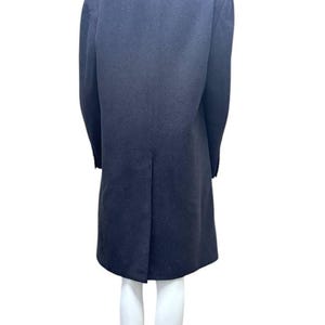 May include: A long, dark blue coat with a high collar and a single back vent. The coat is on a white mannequin.