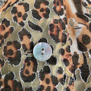 May include: Close-up of a brown and black leopard print fabric with a white button. The fabric has a mesh-like texture.