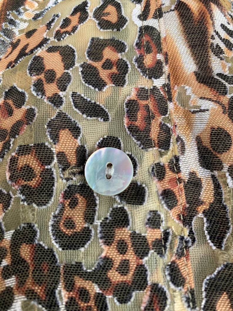 May include: Close-up of a brown and black leopard print fabric with a white button. The fabric has a mesh-like texture.