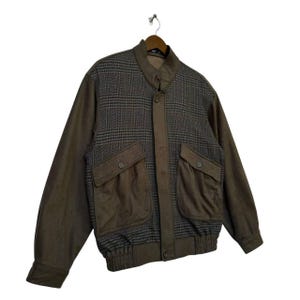 May include: A brown and gray plaid jacket with a zipper closure and two large pockets. The jacket has a ribbed waistband and cuffs.