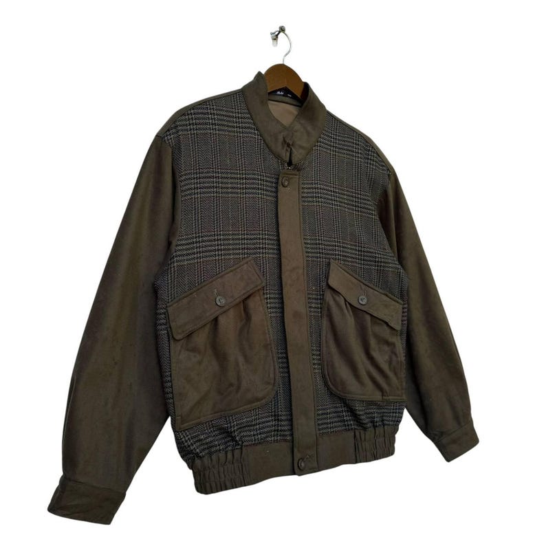 May include: A brown and gray plaid jacket with a zipper closure and two large pockets. The jacket has a ribbed waistband and cuffs.