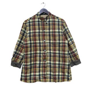 May include: A long-sleeved plaid shirt with a mandarin collar and button closure. The shirt has a brown, red, and yellow plaid pattern and brown leather trim on the cuffs.