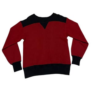 May include: A red and black sweatshirt with a crew neck. The top of the shoulders and the bottom hem are black. The sleeves have black cuffs. The sweatshirt has a V-shaped detail at the neckline.