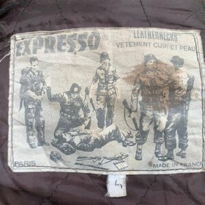 May include: A brown leather jacket with a patch that says "Expresso Leathernecks Vetement Cuir et Peau Paris Made in France". The patch features a black and white illustration of five soldiers.