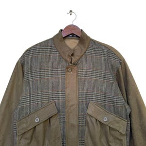 May include: A brown jacket with a plaid pattern on the upper half and a solid brown color on the lower half. The jacket has a zipper closure and two large pockets on the front.