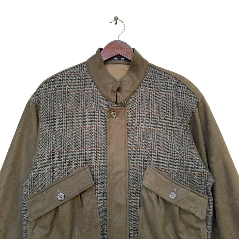 May include: A brown jacket with a plaid pattern on the upper half and a solid brown color on the lower half. The jacket has a zipper closure and two large pockets on the front.