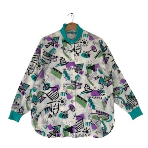 May include: A white long-sleeved button-up shirt with a colourful abstract print featuring geometric shapes, suns, and figures. The shirt has a teal collar and cuffs.
