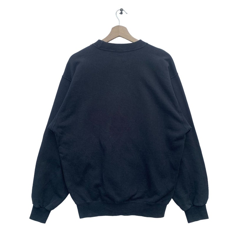 K&ouml;nnte beinhalten: Ein schwarzer Rundhals-Pullover mit langen &Auml;rmeln und geripptem Saum.