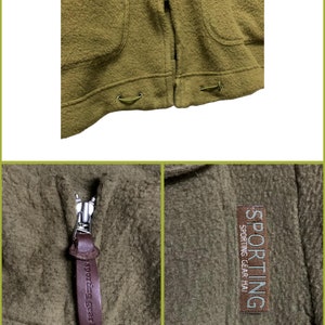 K&ouml;nnte beinhalten: Eine braune Fleecejacke mit Rei&szlig;verschluss und einem braunen Leder-Rei&szlig;verschluss-Zipper. Der Rei&szlig;verschluss-Zipper hat den Text "Sporting Gear Hai" darauf. Die Jacke hat einen Aufn&auml;her auf der Brust mit dem Text "Sporting Gear Hai" in wei&szlig;en Buchstaben auf braunem Hintergrund.