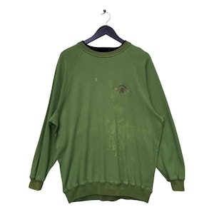 Pode incluir: Camisola verde com gola preta e um logotipo desbotado que diz "Goofy" na frente.