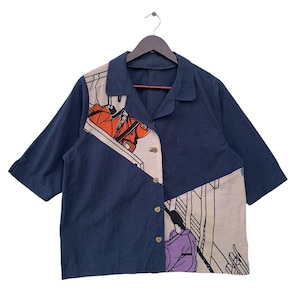 May include: A navy blue short-sleeved button-up shirt with a white and beige patterned design. The pattern features a geometric design with a person in a red and orange outfit and another person in a purple outfit.