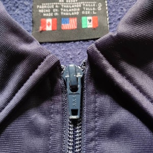 May include: A navy blue zipper with a metal pull. The zipper is partially closed and has a textured fabric background. The zipper is labeled with the letters "XXX".