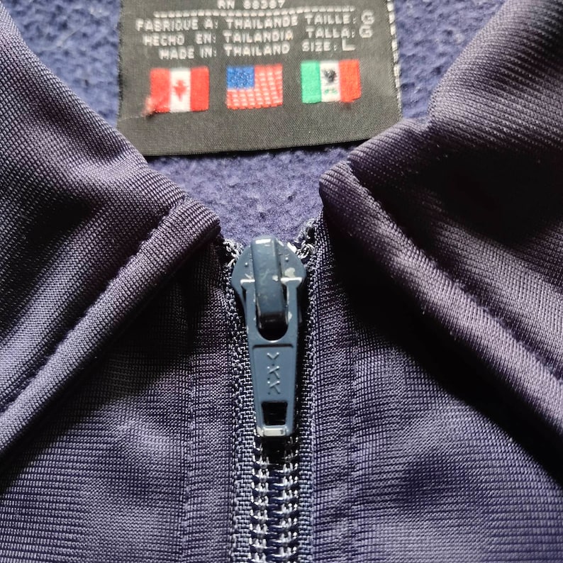 May include: A navy blue zipper with a metal pull. The zipper is partially closed and has a textured fabric background. The zipper is labeled with the letters "XXX".