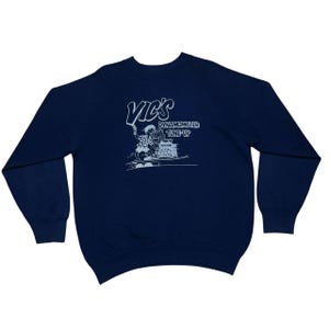 May include: Navy blue sweatshirt with a white graphic that reads "Vic's Dynamometer Tune-Up". The graphic depicts a mechanic working on a machine. The sweatshirt has long sleeves and a crew neck.