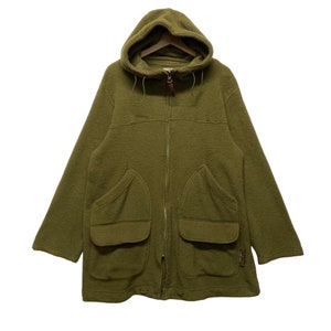 K&ouml;nnte beinhalten: Eine gr&uuml;ne Kapuzenjacke mit Rei&szlig;verschluss und zwei gro&szlig;en Taschen auf der Vorderseite. Die Jacke ist aus einem weichen, flauschigen Material.