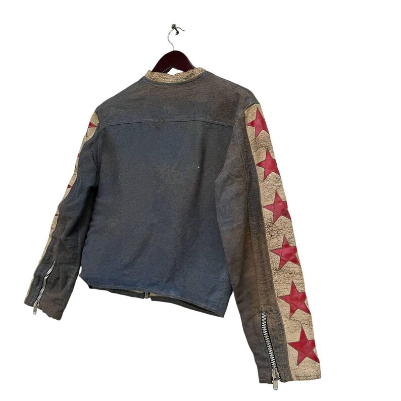 Op de afbeelding: Een blauw denim jack met rode sterren op de mouwen. Het jack heeft een ritssluiting en een opstaande kraag.