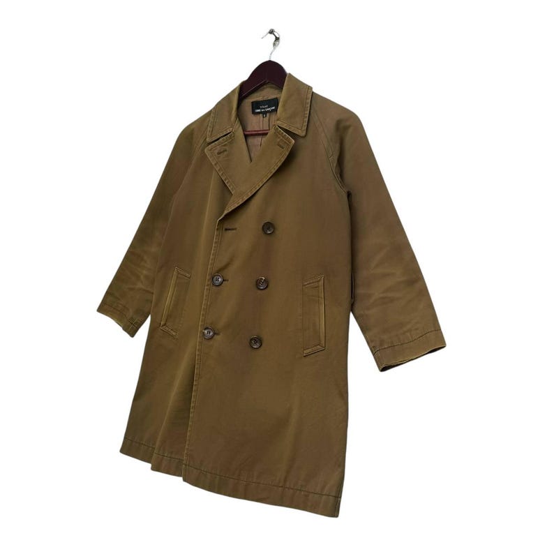 May include: An olive-brown double-breasted trench coat hangs on a wooden hanger. The coat has a notched collar, two rows of buttons, and side pockets. The coat is made of a durable fabric, suitable for various weather conditions.