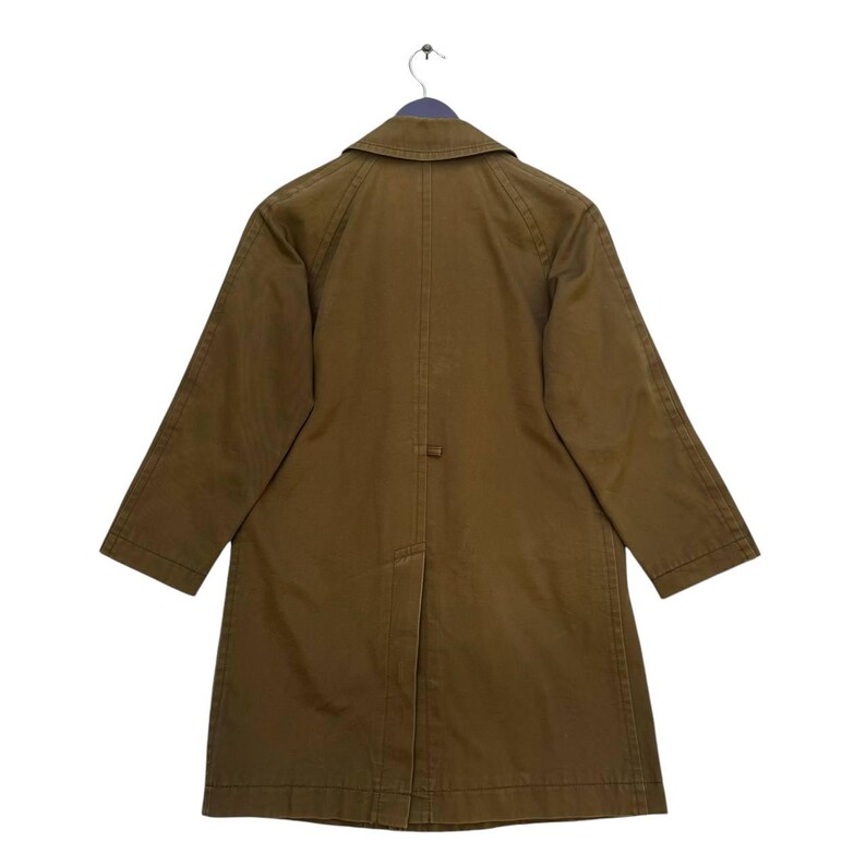 May include: An olive-green coat, hanging from a hanger, is set against a white backdrop. The coat features a traditional collar, long sleeves, and a button fastening. The rear view reveals tailored seams and a vent at the hem.