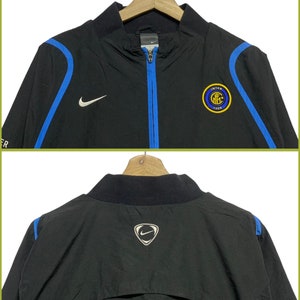 May include: Black Nike windbreaker jacket with blue accents and the Inter Milan logo on the front. The back of the jacket has a Nike swoosh logo.