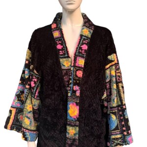 May include: A black, textured robe with colorful patterned trim and sleeves. The trim features pink, yellow, blue, and green geometric designs. The robe is displayed on a mannequin.