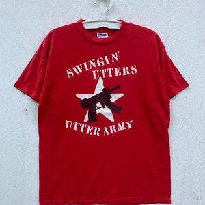 Może przedstawiać: Czerwony T-shirt z białą gwiazdą i czarną sylwetką pistoletu. Na koszulce nadrukowany jest tekst "Swingin' Utter's Utter Army".