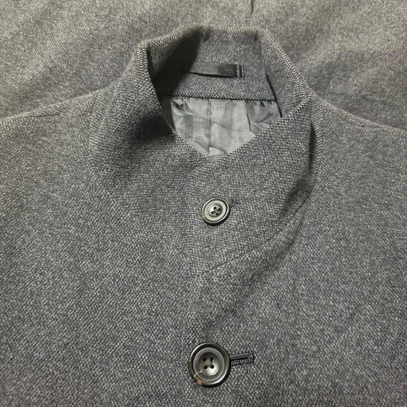 Vintage Mens black wool blend long overcoat featuring a minimalist button up design with stand collar made by A.A.R Durban Urban.Vintage coat ideal for fall and winter streetwear,office wear or layered casual looks.Classic and sleek,perfect for fashion forward individuals seeking timeless urban outerwear.This stylish trench style coat offers comfort,warmth and elegance for everyday city life or formal occasions.