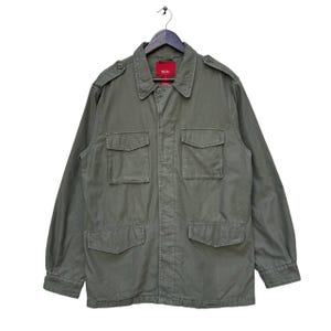 May include: A green utility jacket with a red label that says "Wrangler" on the left side of the chest. The jacket has four pockets on the front and a button closure.