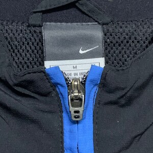 May include: A black zippered jacket with a blue stripe down the front. The jacket has a mesh lining and a Nike logo on the tag. The tag also says "M" and "Made in Indonesia".