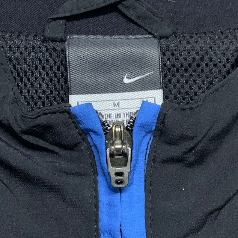 May include: A black zippered jacket with a blue stripe down the front. The jacket has a mesh lining and a Nike logo on the tag. The tag also says "M" and "Made in Indonesia".