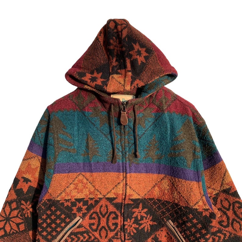 May include: A multi-colored hooded jacket with a zipper closure. The jacket features a geometric pattern with shades of orange, red, green, blue, and purple. The hood is lined with a black and brown pattern.