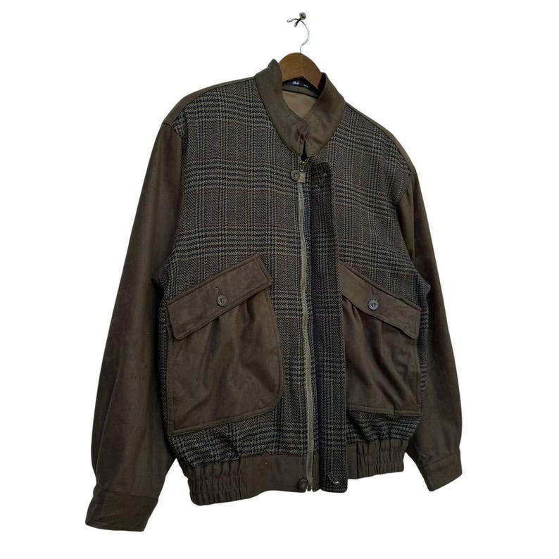 May include: A brown and black plaid jacket with a zipper closure and two large pockets. The jacket has a brown suede-like material on the pockets and sleeves.