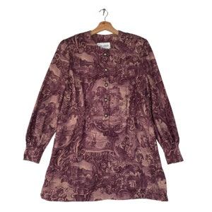Puede incluir: Una camisa de manga larga con botones y un estampado toile morado y beige. La camisa tiene un cuello mandarín y un corte holgado.