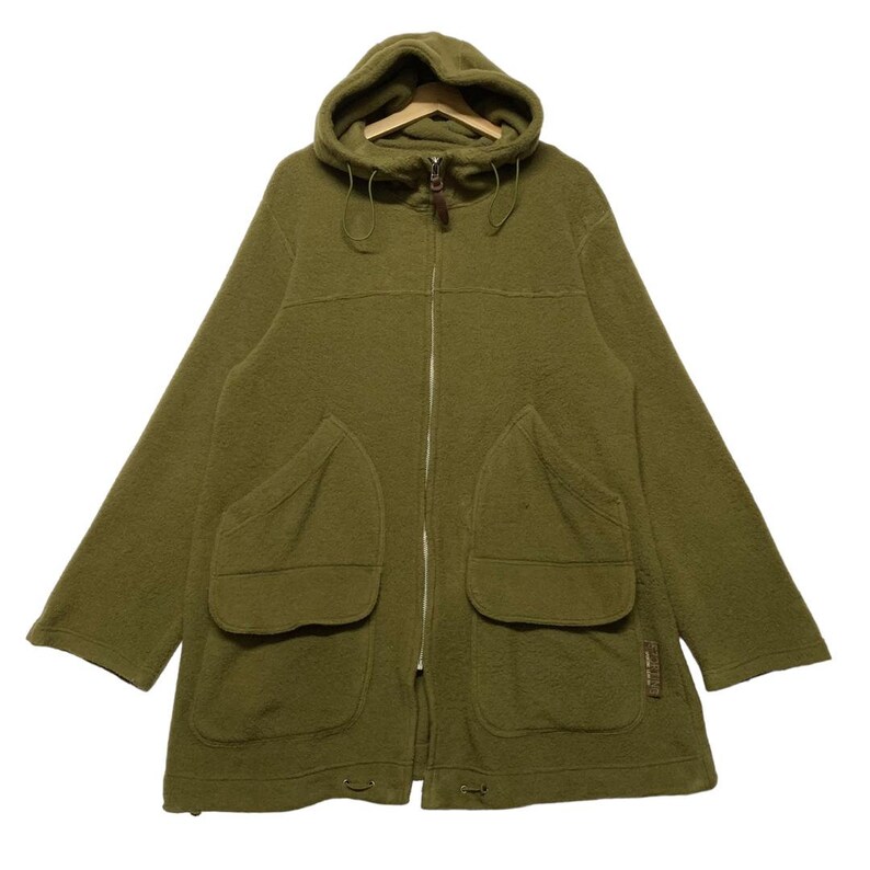 K&ouml;nnte beinhalten: Eine gr&uuml;ne Kapuzenfleecejacke mit Rei&szlig;verschluss und gro&szlig;en Taschen. Die Jacke hat eine Kapuze mit Kordelzug und einen braunen Rei&szlig;verschluss.