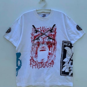 May include: White t-shirt with a graphic print of a face with crossed skateboards and the text "Don't mess with Texas". The graphic is in red, black, and blue. The shirt also has a smaller graphic on the right sleeve with the text "HEX".