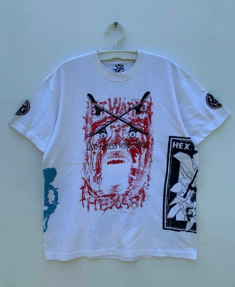 May include: White t-shirt with a graphic print of a face with crossed skateboards and the text "Don't mess with Texas". The graphic is in red, black, and blue. The shirt also has a smaller graphic on the right sleeve with the text "HEX".