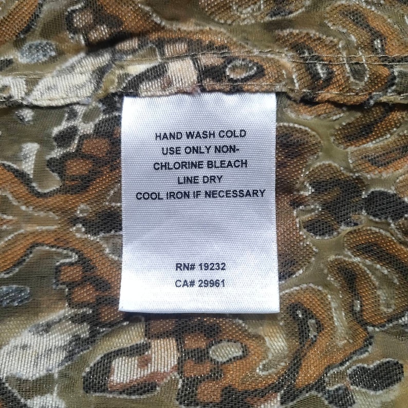 May include: White care label with instructions for washing and ironing a garment. The label reads "HAND WASH COLD, USE ONLY NON-CHLORINE BLEACH, LINE DRY, COOL IRON IF NECESSARY". The label also includes the following information: RN# 19232, CA# 29961.