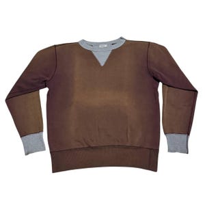 May include: A long-sleeve sweatshirt featuring a dark brown body with a faded center. The garment includes a light gray ribbed crew neckline with a V-shaped insert, matching light gray ribbed cuffs, and a wide light gray ribbed hem at the bottom.