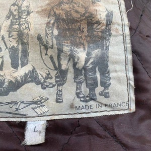 May include: A close-up of a brown leather jacket with a white label sewn into the inside. The label features a black and white illustration of soldiers and the text "Made in France".