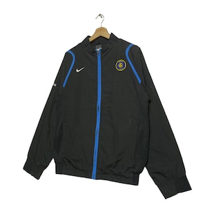 May include: Black windbreaker jacket with blue accents and a zipper closure. The jacket features a team logo on the left chest and a Nike swoosh logo on the right chest.