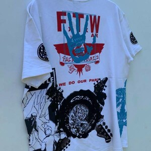 May include: White t-shirt with a graphic print of a hand with the text "FTW" and "4 year anniversary" and "FUCK THE WORLD". The shirt also has a graphic print of guitars and the text "WE DO OUR PART" and "GO SKATE".