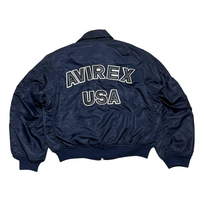 Vintage Avirex MA 1 Bomber Jacket Navy USA Flight Jacket 90s Streetwear Military Jacket Classic Zip Up Nylon Bomber Coat For Men And Women Rare Avirex USA Outerwear Piece With Iconic Back Logo Design.